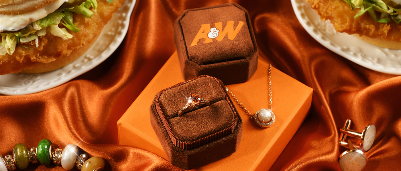 Orange diamond ring in a brown box, charm bracelet, and a necklace surrounded by two Cod Sandwiches